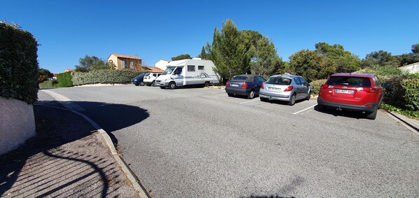 Een parkeerplaats met meerdere voertuigen, waaronder een camper, een zilveren sedan en een rode SUV.