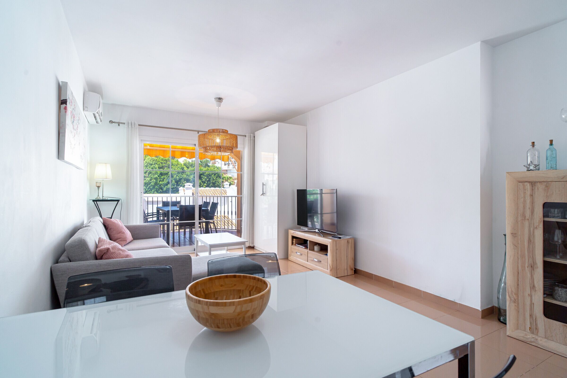 A modern living room with a sofa, TV, dining table, and a view of the outdoors.