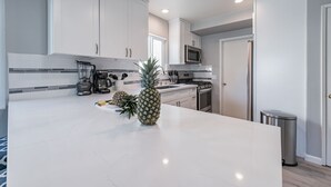 A modern kitchen with white cabinets, a large island, a microwave, and a trash can. - The Pineapple Suite, Whitewater Views steps to Sand  (San Clemente)