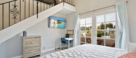 A bedroom with a large bed, a desk, and a staircase.