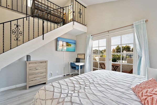 A bedroom with a large bed, a desk, and a staircase.