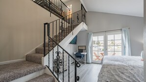 A bedroom with a large bed, a desk, and a staircase with a railing. - The Pineapple Suite, Whitewater Views steps to Sand  (San Clemente)