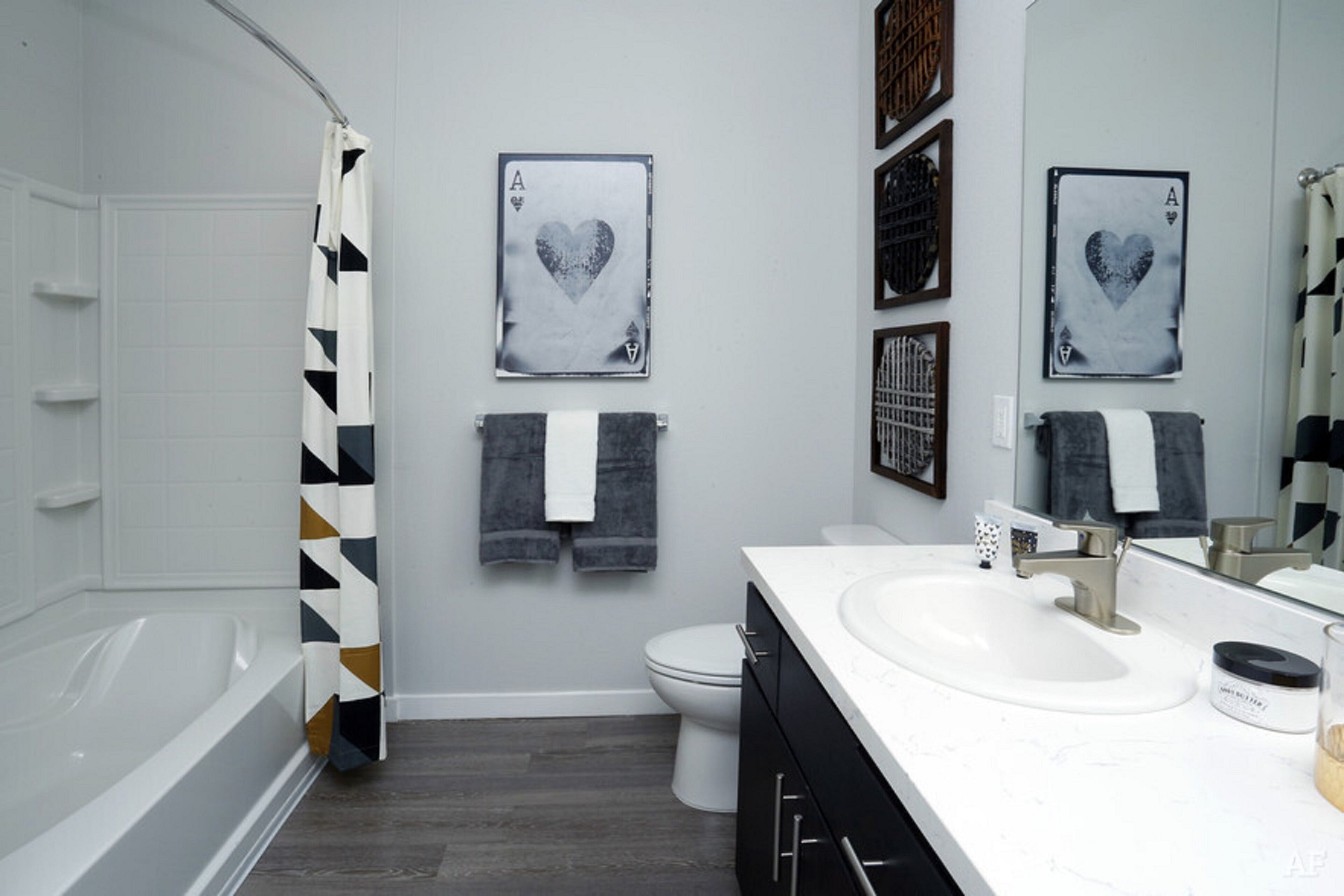 A modern bathroom with a bathtub, toilet, and sink. There are two framed playing cards with hearts on the wall.