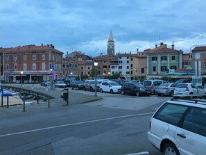 Vista da rua com carros estacionados, edifícios e uma torre ao fundo.