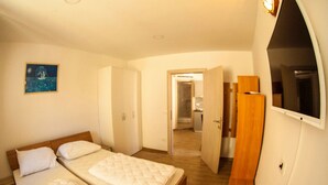 Ein Schlafzimmer mit zwei Betten, einem Holzschrank, einem Fernseher und einem durch eine offene Tür erreichbaren Badezimmer.