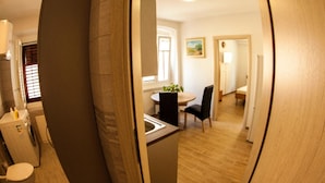 Eine moderne Küche mit integriertem Geschirrspüler, eine Essecke mit rundem Tisch und Stühlen sowie ein Flur, der zum Schlafzimmer führt.