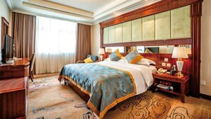 A hotel room with a large bed, a desk, and a nightstand with a lamp. - Mianzhou Hotel (Mianyang)