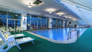 An indoor swimming pool with a skylight ceiling, lounge chairs, and a green floor. - Mianzhou Hotel (Mianyang)
