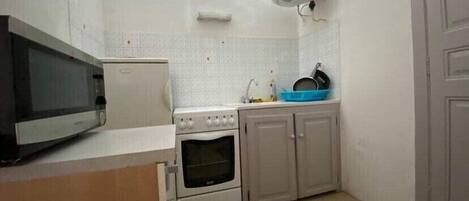 A compact kitchen with a microwave, stove, oven, and a sink with a blue dish rack.