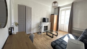 A modern hotel room with a wooden floor, a dining table, a sofa, a TV, a fireplace, and a large window with curtains. - Charming T1 full center Corte 13 cours paoli free wifi quiet bright (Corte)