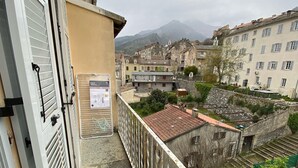 A balcony with a metal railing overlooking a courtyard with buildings and a mountain in the background. - Charming T1 full center Corte 13 cours paoli free wifi quiet bright (Corte)