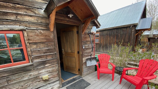 Eine Holzhütte mit Veranda, zwei rote Adirondack-Stühle und einer Fußmatte.
