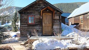 Eine Holzhütte mit Holztür und kleinem Fenster, umgeben von Schnee.