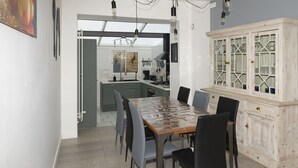 A modern kitchen with a dining area, featuring a large wooden table, grey chairs, and a light wooden cabinet with glass doors. - "Au Coin D'la Rue" Maison Avec Jardin à 2 pas de la Plage (Fécamp)
