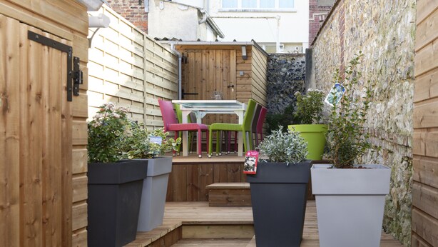 A wooden deck with a table and chairs, surrounded by potted plants and a wooden fence. - "Au Coin D'la Rue" Maison Avec Jardin à 2 pas de la Plage (Fécamp)