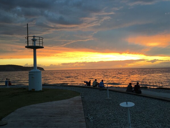 A coastal sunset view with a lighthouse, a pebble path, and people sitting on benches. - Apartment Lighthouse &free Parking in Izola-isola (Izola)