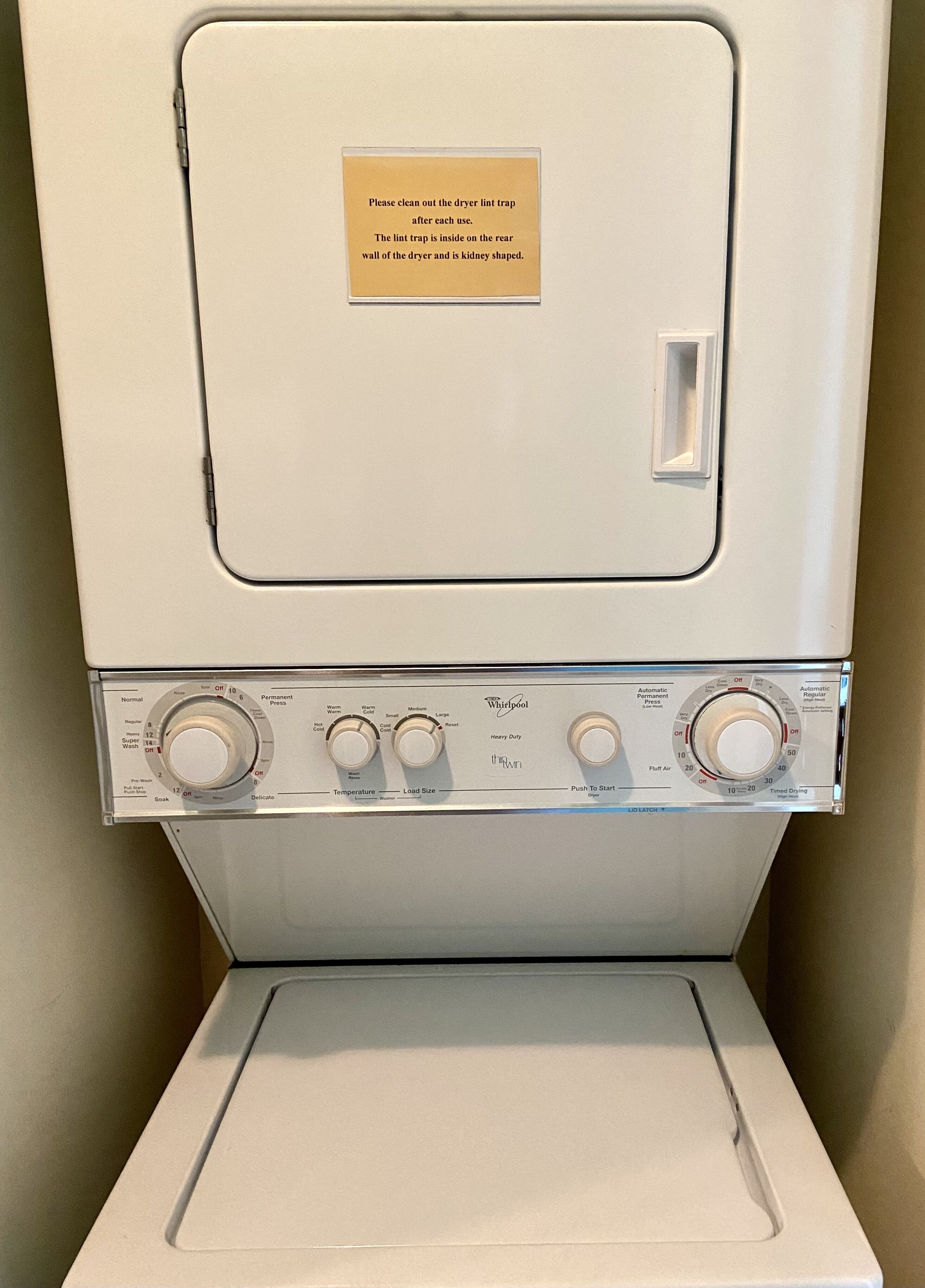 A front view of a Whirlpool dryer with control knobs and a label instructing to clean the lint trap after each use.