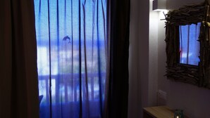A room with a large window covered by sheer curtains, a wall-mounted mirror, and a small wooden table with a candle. - Panorama Gennadi (Rhodes)