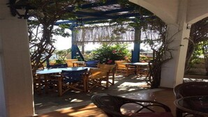 An outdoor patio area with wooden tables and chairs, covered by a blue pergola with hanging vines. - Panorama Gennadi (Rhodes)