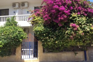 Un edificio con balcón, una reja y un arbusto grande florecido.