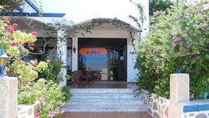 A hotel entrance with steps leading up to a door, a sign indicating all rooms are air-conditioned, and a stone wall with plants on either side. - Panorama Gennadi (Rhodes)
