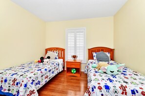 Una habitación con dos camas, cada una con cabecero de madera, una mesita de noche con lámpara y una ventana con contraventanas.