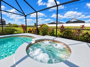 A pool area with a hot tub, surrounded by a metal fence and lush greenery.