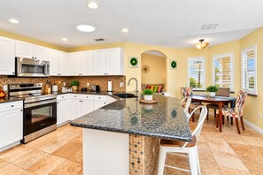 A kitchen with white cabinets, stainless steel appliances, a granite countertop, and a dining area with a table and chairs.