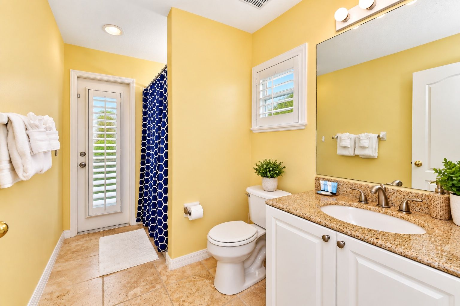 A bathroom with yellow walls, a white toilet, a sink with a granite countertop, and a mirror above the sink.