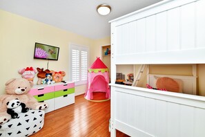 Una sala de juegos infantil con una tienda de campaña rosa, un oso de peluche grande y varios juguetes.