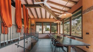 Uma sala de jantar com uma mesa comprida, cadeiras, um ventilador de teto e janelas grandes.