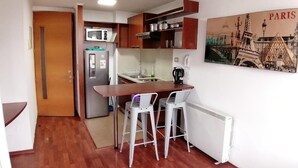 A compact kitchen with a microwave, refrigerator, and a small dining area with two chairs. - Santiago Moneda Suites 1802 (Santiago)