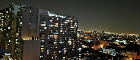 A high-rise building with multiple illuminated windows, likely a hotel or apartment complex, with a view of the cityscape at night.