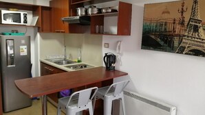 A compact kitchen with a microwave, stove, and sink. There is a painting of the Eiffel Tower on the wall. - Santiago Moneda Suites 1802 (Santiago)