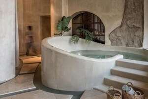 A spa area with a large bathtub, steps leading to a shower area, and a stone wall.