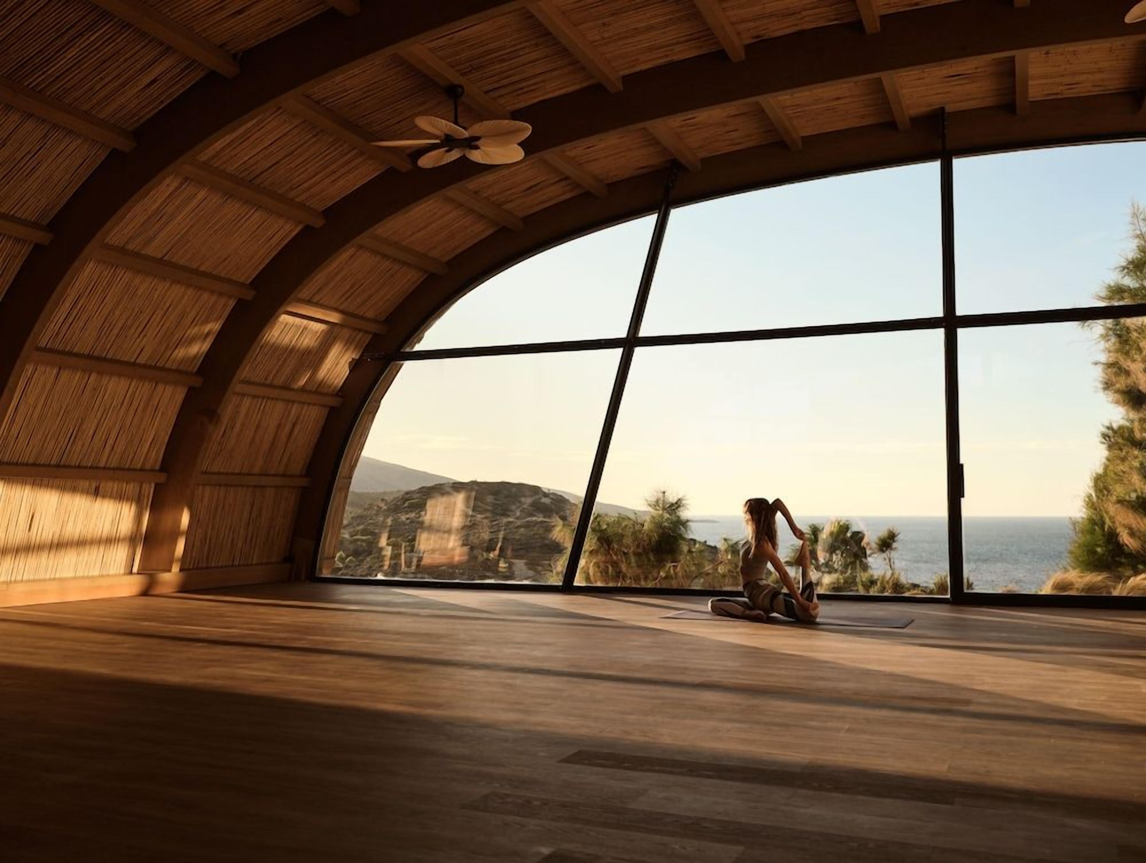 A spacious room with a large arched window offering a view of the sea and hills.