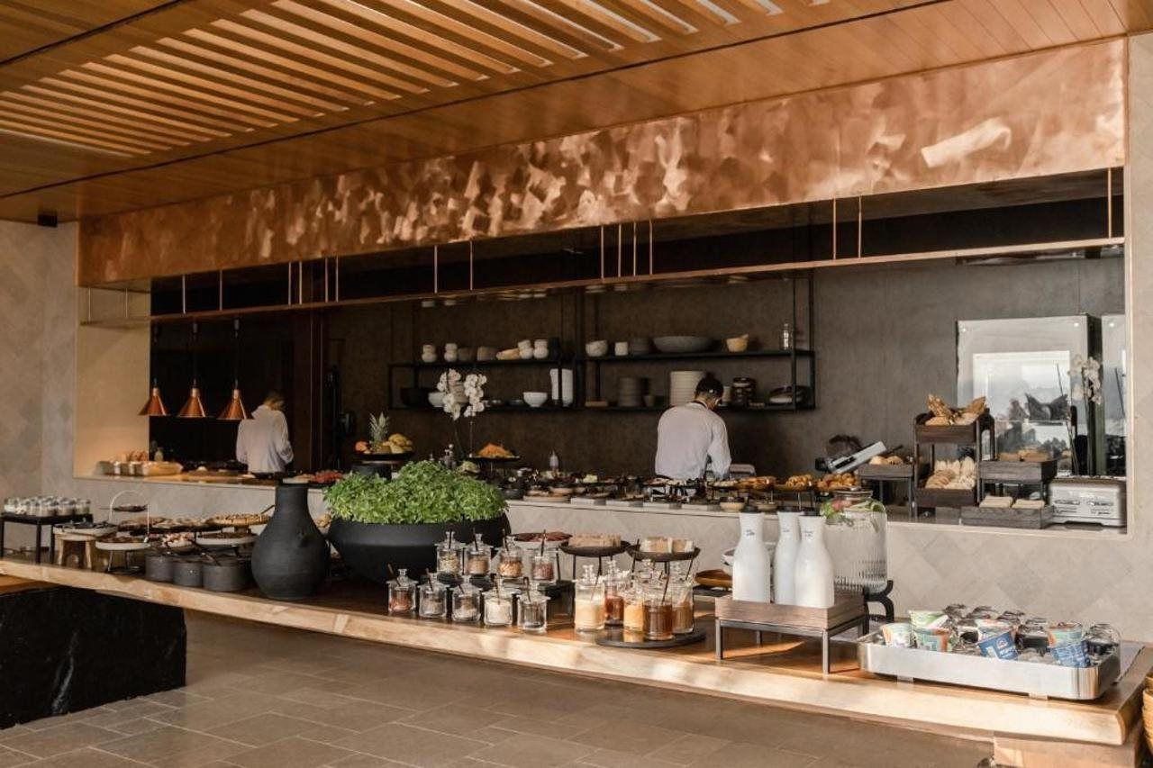 Cocina moderna con chefs preparando alimentos, una variedad de utensilios de cocina y una exhibición de productos alimenticios.
