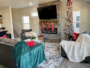 Un salon chaleureux avec une cheminée, un sapin de Noël et un téléviseur à écran plat fixé au-dessus de la cheminée.
