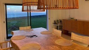 Comedor con una gran mesa de madera, individuales tejidos y vistas al mar a través de amplios ventanales.