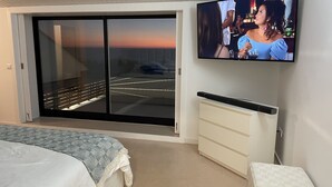 Un dormitorio con cama, televisor montado en la pared, puerta corrediza de vidrio que da a un balcón y una mesita de noche.