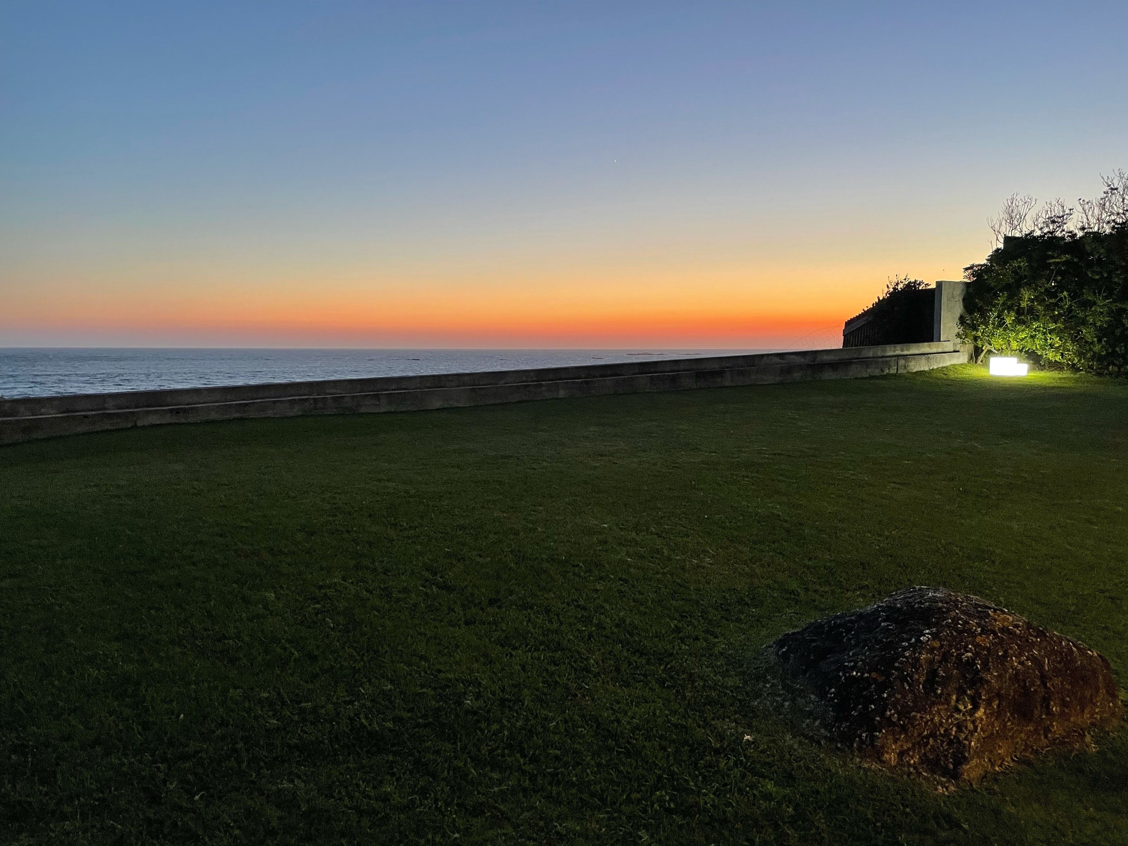 A grassy area with a concrete barrier and a large rock in the foreground.