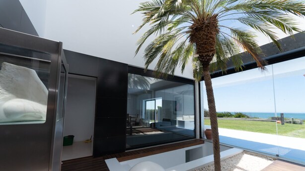 Un espacio habitable moderno y abierto con pared de vidrio con vista a una piscina y al océano.