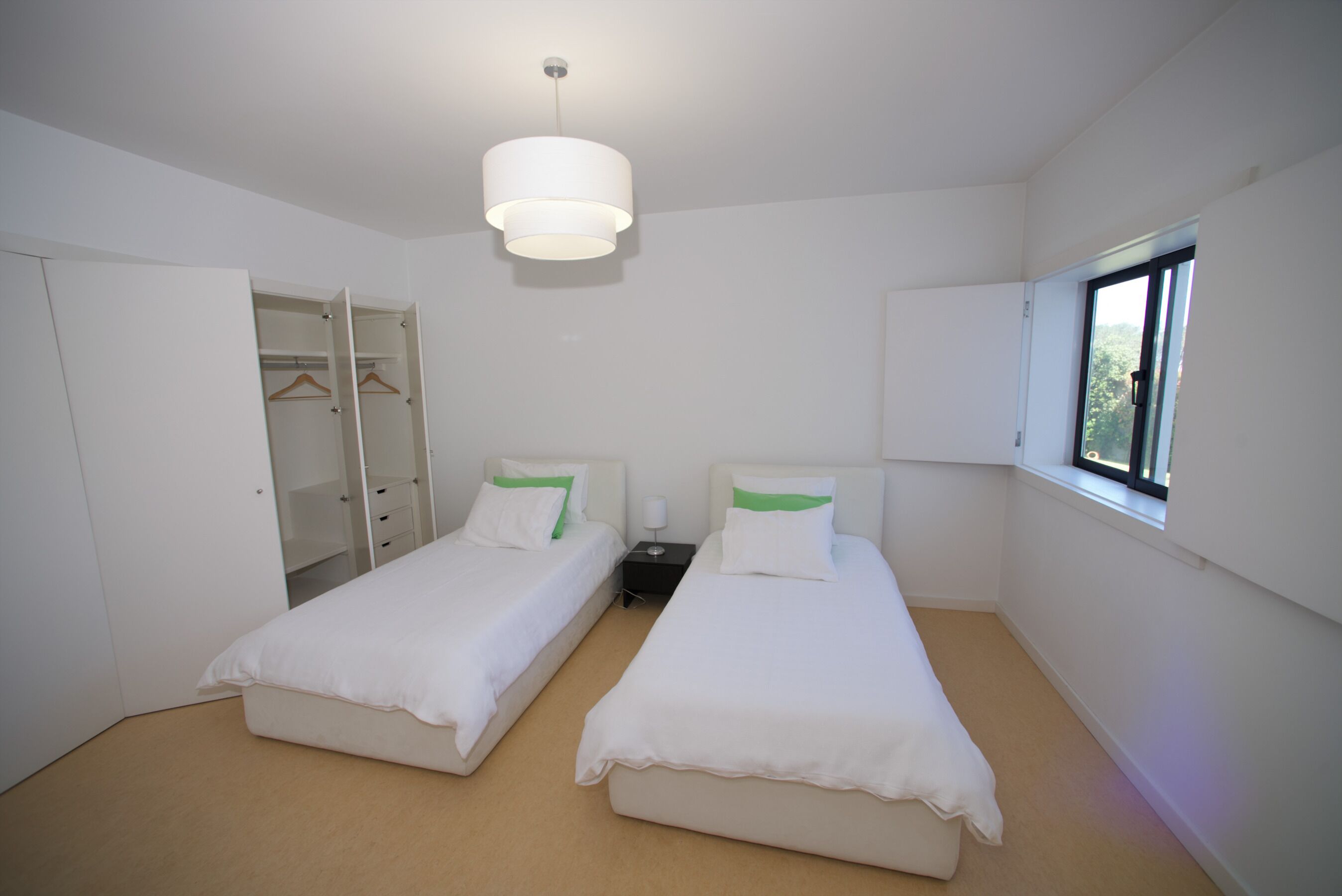 Ein Zimmer mit zwei Betten, einem Kleiderschrank, einem Nachttisch und einem Fenster.