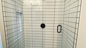 Shower area features a grid-patterned tile floor and walls, a central drain, and a glass door with a black handle.