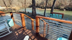 Una terraza de madera con barandilla que da a un río, rodeada de árboles.