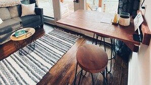 Una sala de estar acogedora con un sofá, una mesa de centro y una mesa de comedor con sillas. Hay un ventanal con vistas a árboles y una terraza afuera.