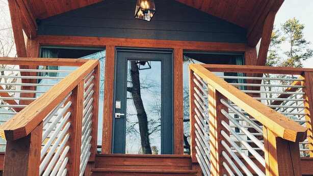Una escalera de madera lleva a una cabaña con techo oscuro y una lámpara colgante.