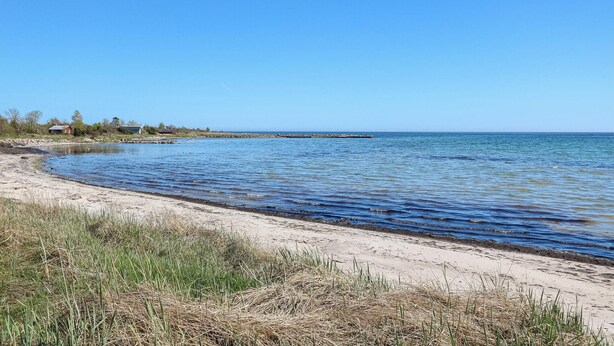 A beach with clear blue water, a sandy shore, and a distant pier. - Beautiful home in Löttorp with WiFi (Löttorp)