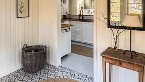 A hallway with a wicker basket, a patterned floor, a wooden console table with a lamp, and a mirror. - 3 bedroom stunning home in Hornbæk (Hornbæk)