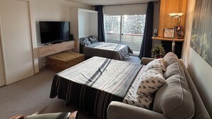 A room with two beds, a TV, a wooden cabinet, and a window with curtains. - Big White Ski-In Ski-Out at Ponderosa in Village (Big white)